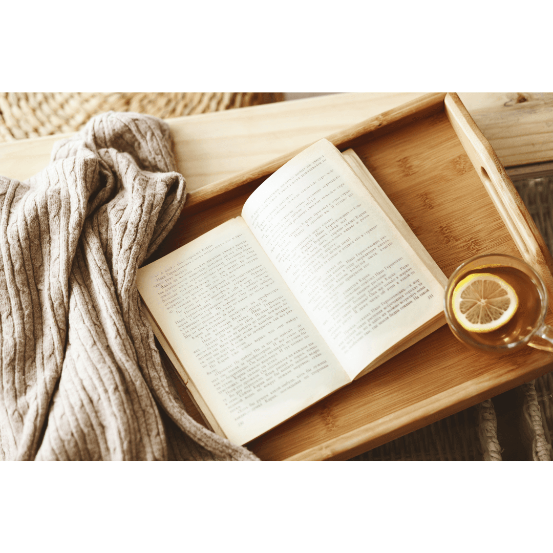Vue de haut d'un livre ouvert sur un plateau en bois avec une tasse de thé au citron et un jeté en laine douillet