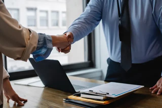 Gros plan de deux professionnels s'accordant sur un contrat par une poignée de main au-dessus d'un bureau avec ordinateur et documents