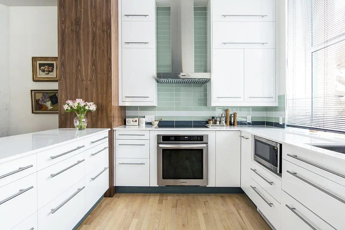 Cuisine contemporaine et lumineuse avec îlot central, plan de travail en quartz blanc et armoires blanches. L'escalier en métal noir ajoute une touche industrielle à cet espace ouvert sur le salon. Parfaite pour les amateurs de lofts et d'espaces ouverts.