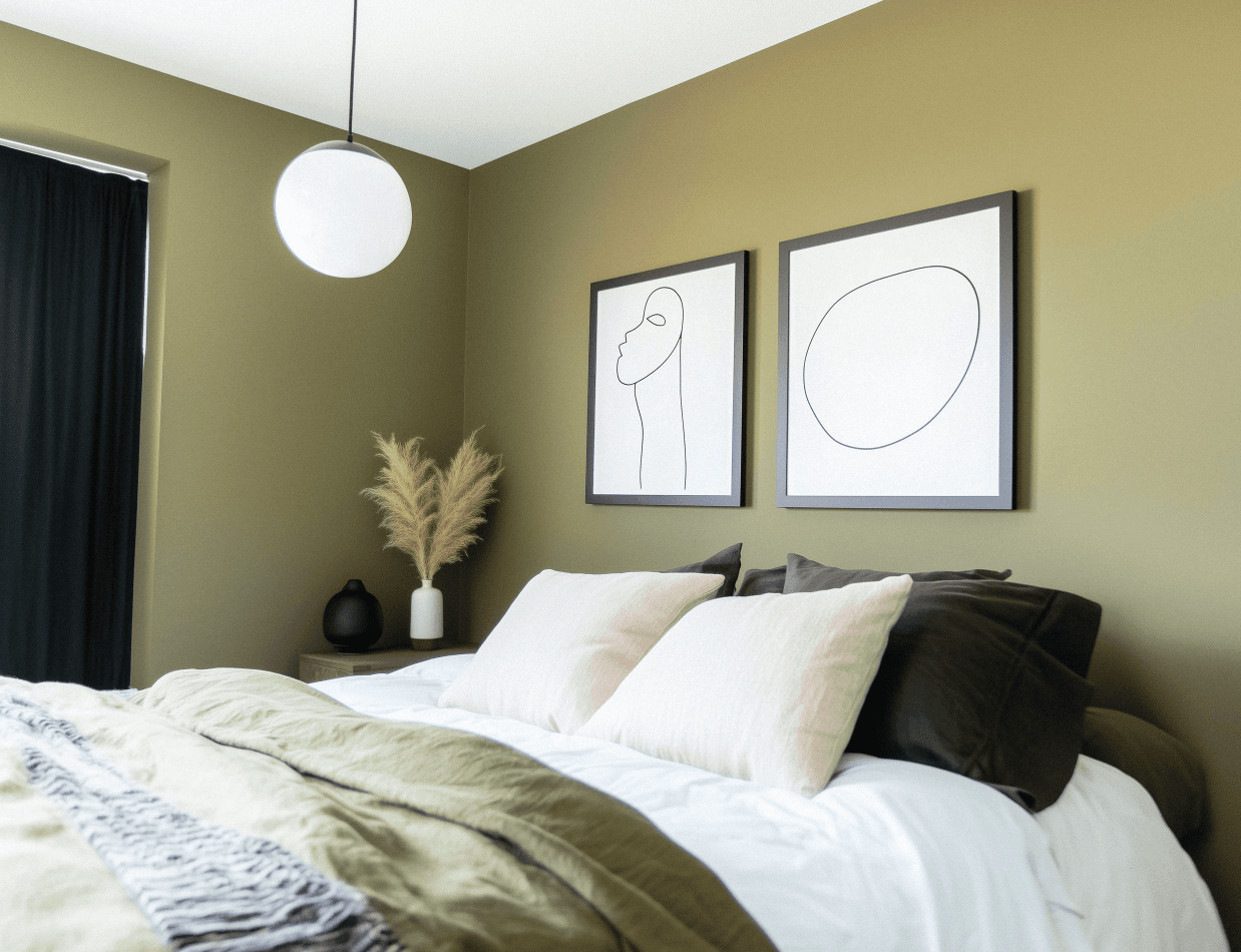 Chambre moderne avec mur vert olive, décor minimaliste, tableaux artistiques en ligne, lit confortable avec coussins beiges et verts, éclairage suspendu sphérique.