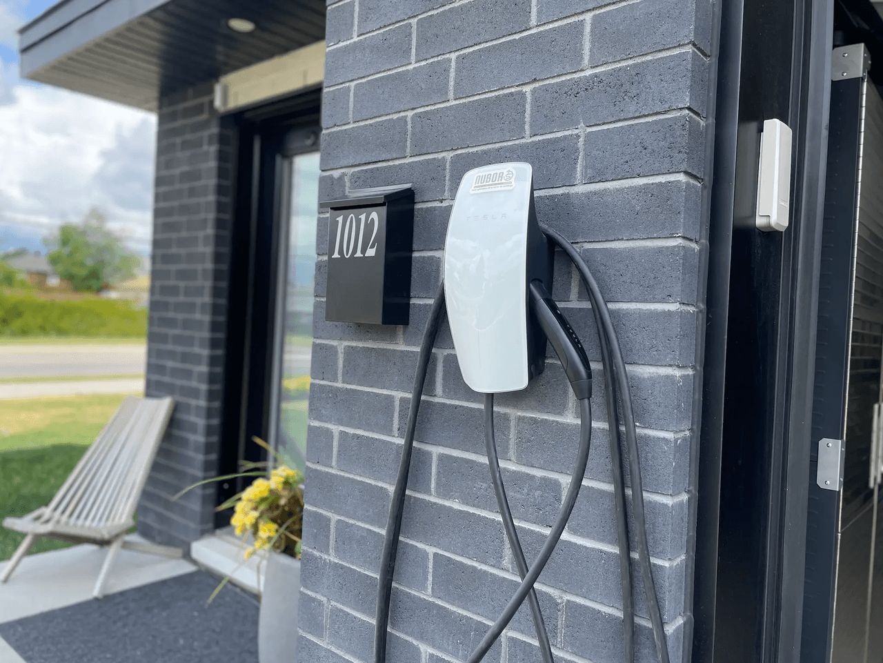 Borne de recharge électrique murale installée sur façade en brique grise moderne à l’entrée d’une maison