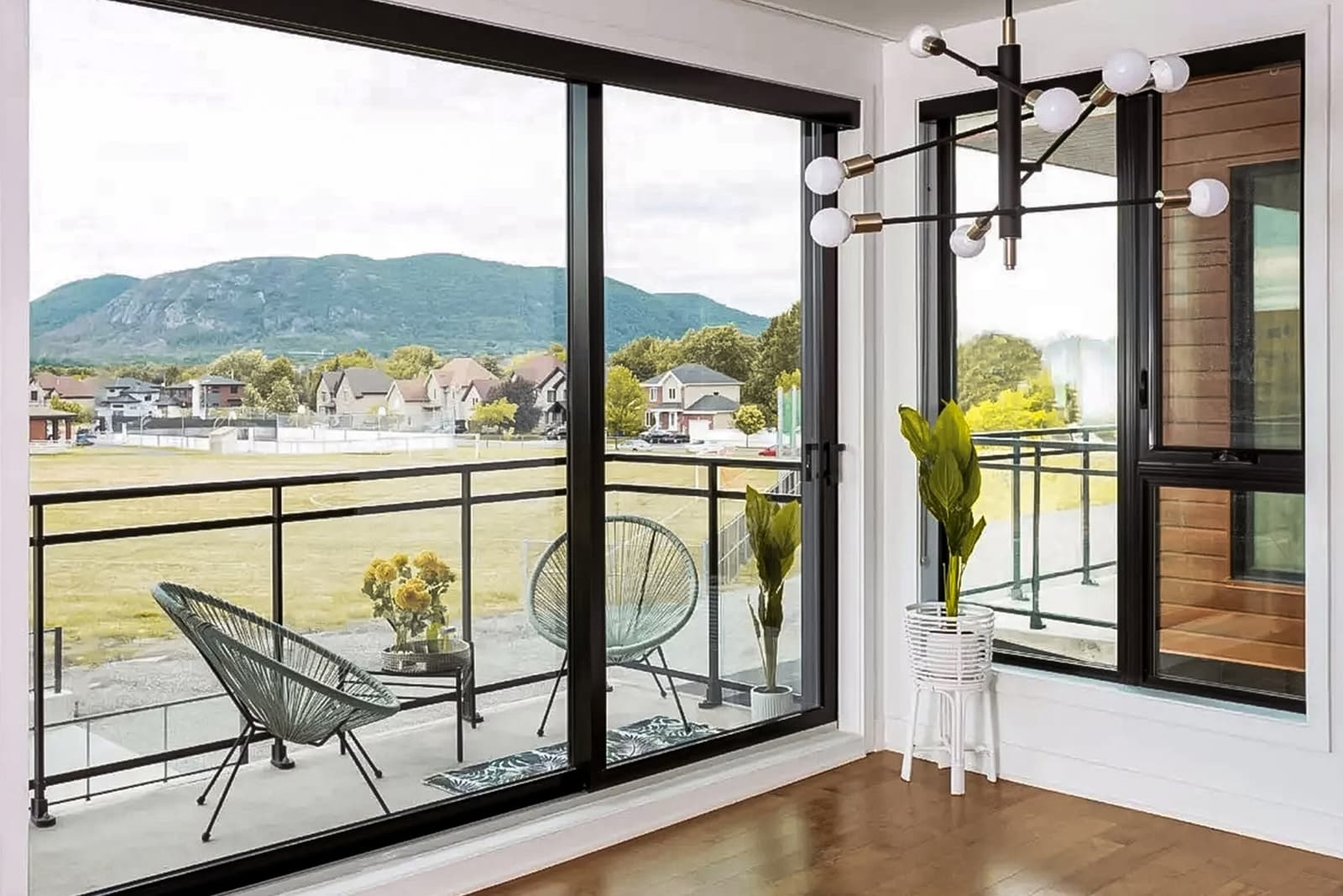 Portes-fenêtres coulissantes modernes offrant une vue panoramique sur un balcon avec mobilier et montagnes en arrière-plan.