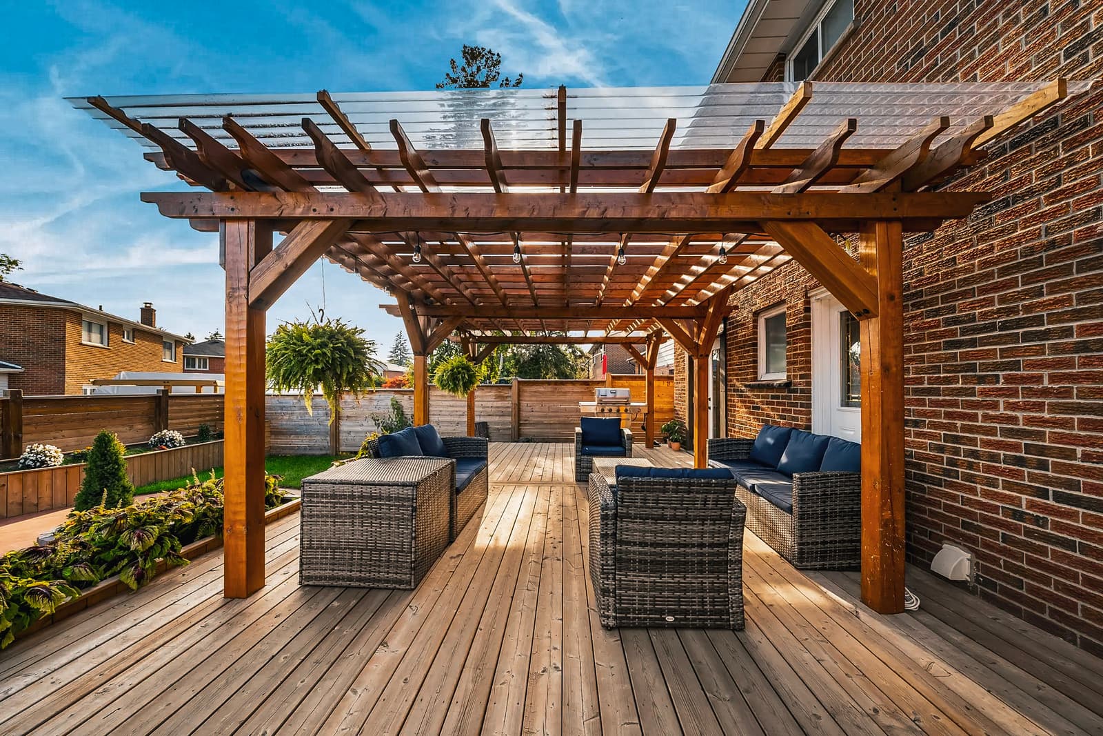Terrasse extérieure moderne avec pergola en bois, mobilier en rotin, coussins bleus, panneaux d'intimité et aménagement paysager élégant.