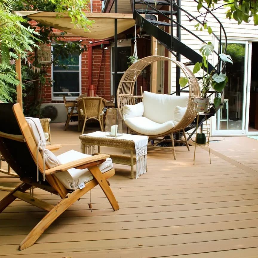 Terrasse en bois avec mobilier en rotin, fauteuil suspendu, fauteuil en bois et décorations végétales, créant une ambiance chaleureuse et relaxante.
