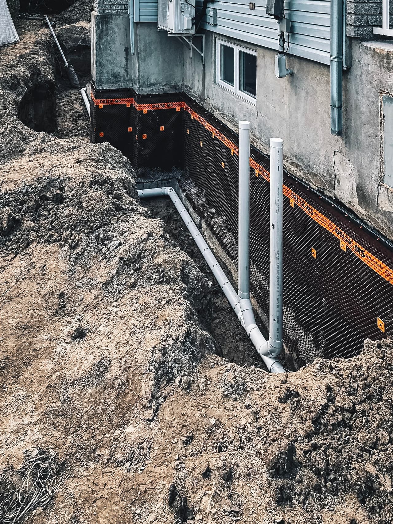 Travaux d'excavation pour l'installation d'un drain français et d'une membrane d'étanchéité sur la fondation d'une maison.