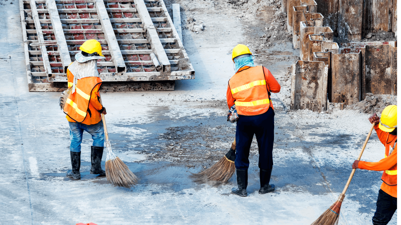Travailleurs de la construction nettoyant un chantier avec balais et portant des équipements de sécurité.
