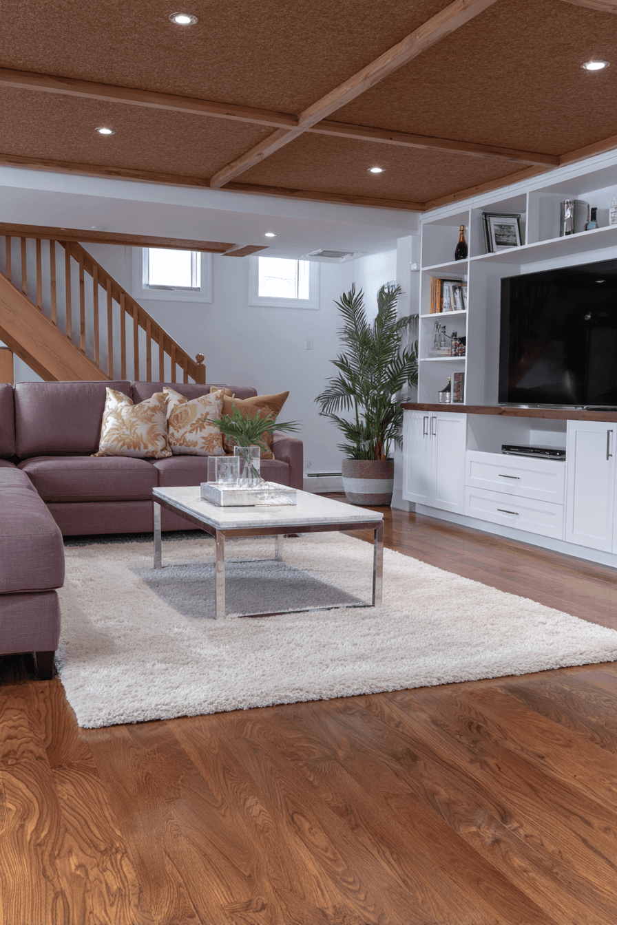 Sous-sol aménagé moderne avec plafond en bois, canapé confortable, meuble télé intégré et plancher de bois