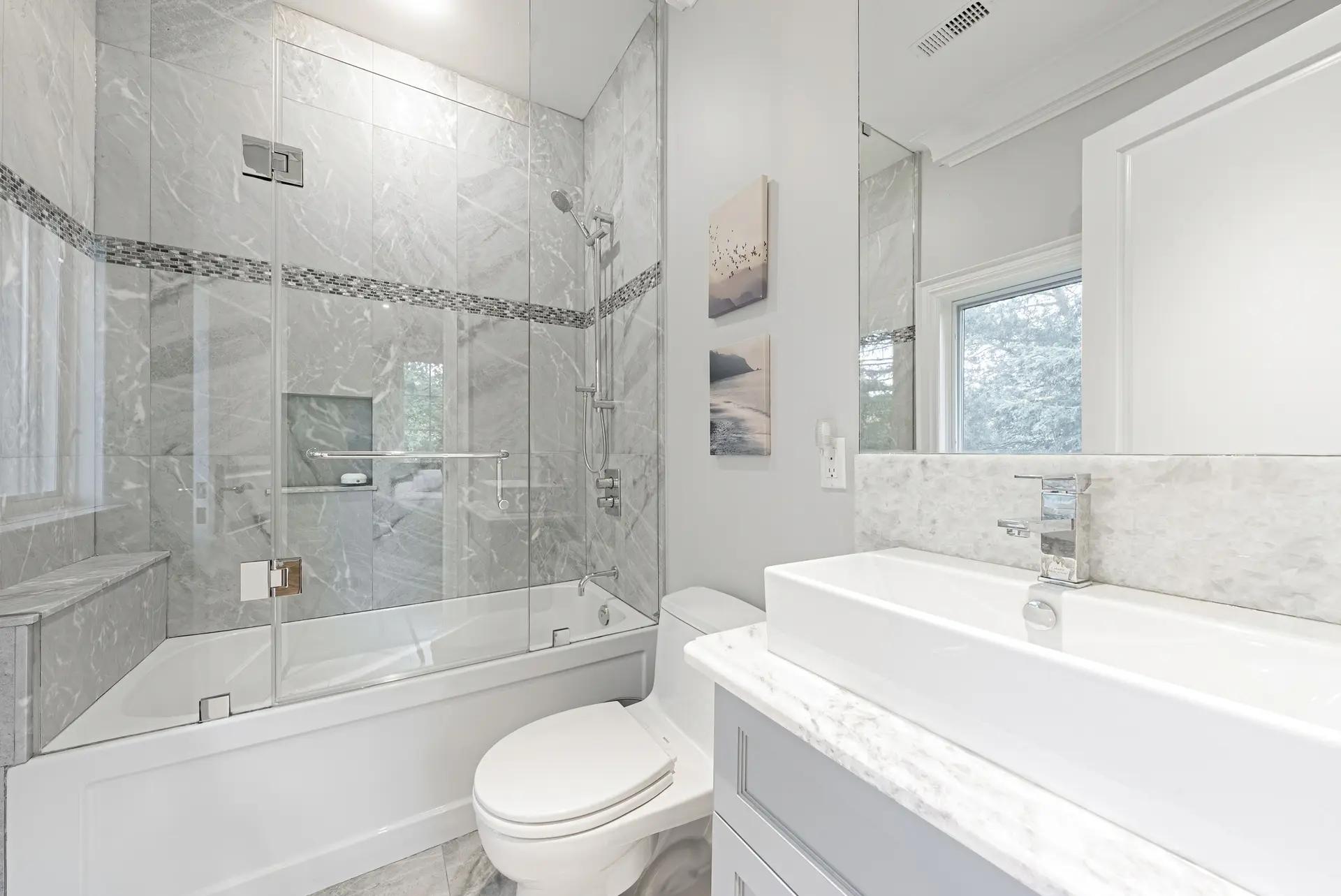 Salle de bain élégante avec une baignoire et une douche séparées par une paroi en verre, un meuble-lavabo flottant et un carrelage en marbre gris clair.