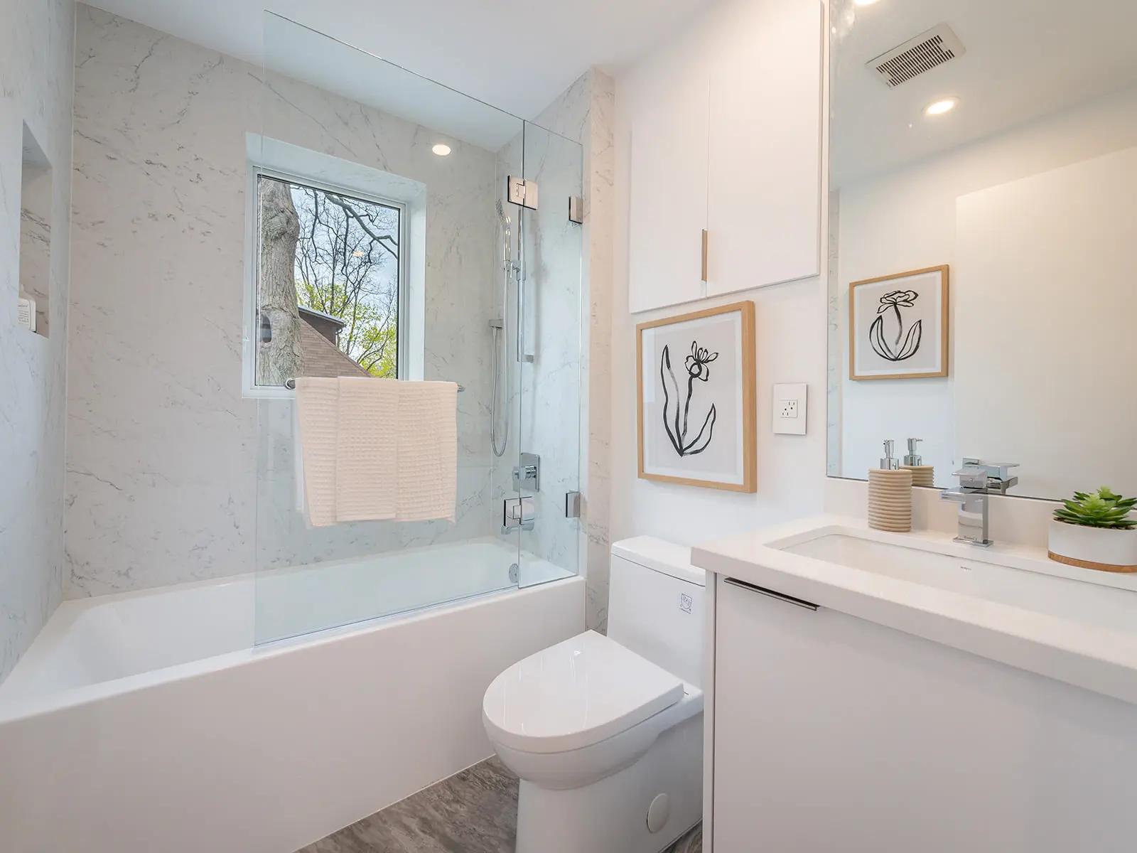 Salle de bain moderne, carrelage imitation bois, baignoire blanche, douche en verre, vasque minimaliste, armoire murale, décoration murale, plantes d'intérieur, ambiance zen.