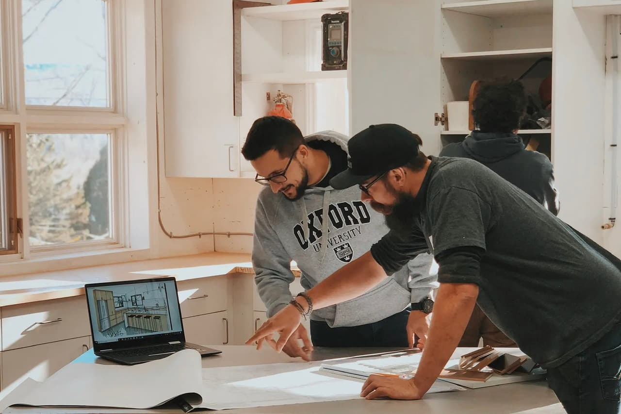 Des professionnels collaborent dans un atelier sur la conception d'un projet architectural avec plans et ordinateur portable.