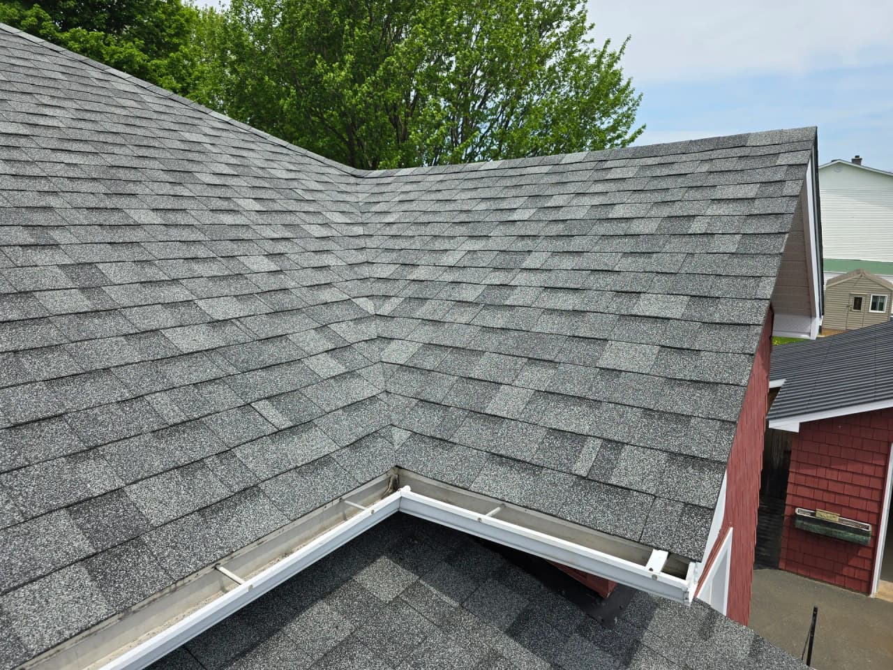 Toiture en bardeaux d'asphalte gris récemment installée avec gouttières blanches sur une maison rouge.