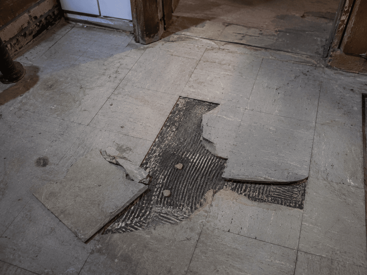 Plancher intérieur endommagé avec carreaux retirés et adhésif noir exposé, préparé pour des travaux de démolition et de remplacement du revêtement