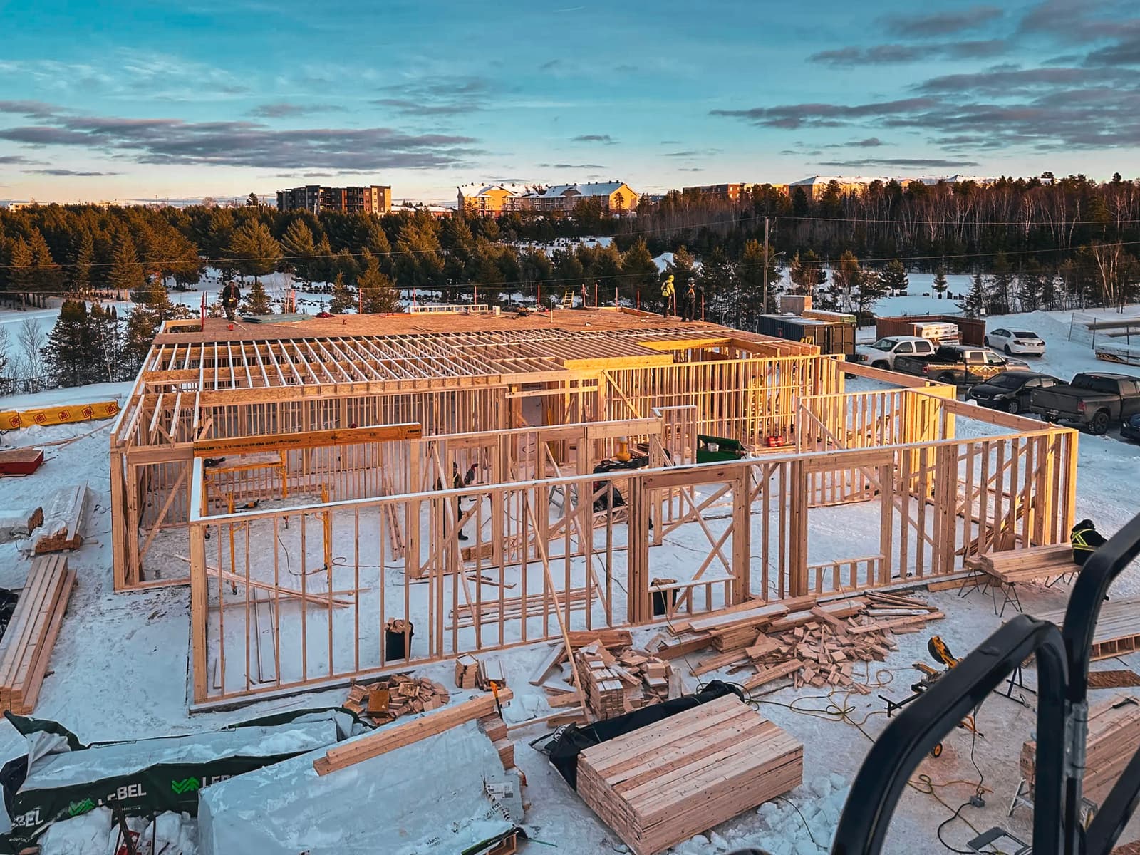 Vue d'un chantier de construction résidentielle avec une charpente en bois en cours de montage sur un site enneigé.