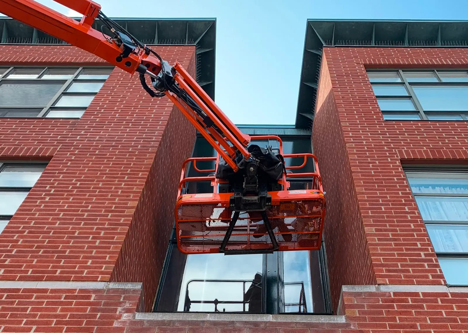 Travaux de rénovation sur un bâtiment en brique rouge avec une nacelle élévatrice utilisée pour accéder aux fenêtres en hauteur.