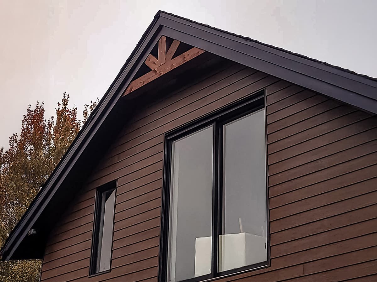 Façade moderne avec revêtement en bois, grandes fenêtres et charpente apparente.