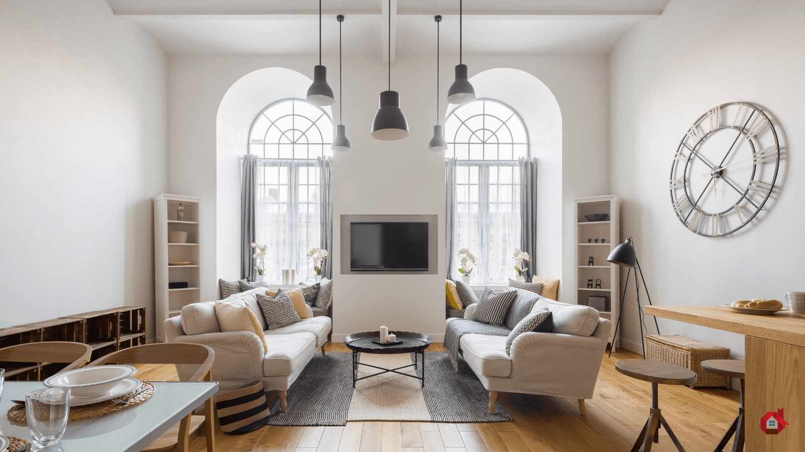 Salon lumineux et contemporain avec hauts plafonds, grand canapé blanc, plancher en bois et grande horloge murale.