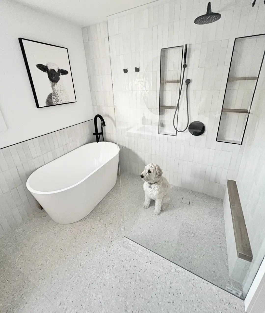 Salle de bain moderne avec baignoire îlot, douche à l'italienne et carrelage en terrazzo. Accompagne d'un petit chien&nbsp;