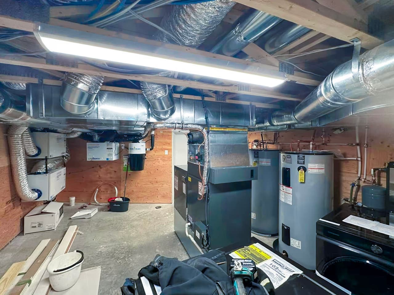 Salle mécanique de sous-sol avec fournaise, chauffe-eau, conduits de ventilation et équipements de chauffage résidentiel