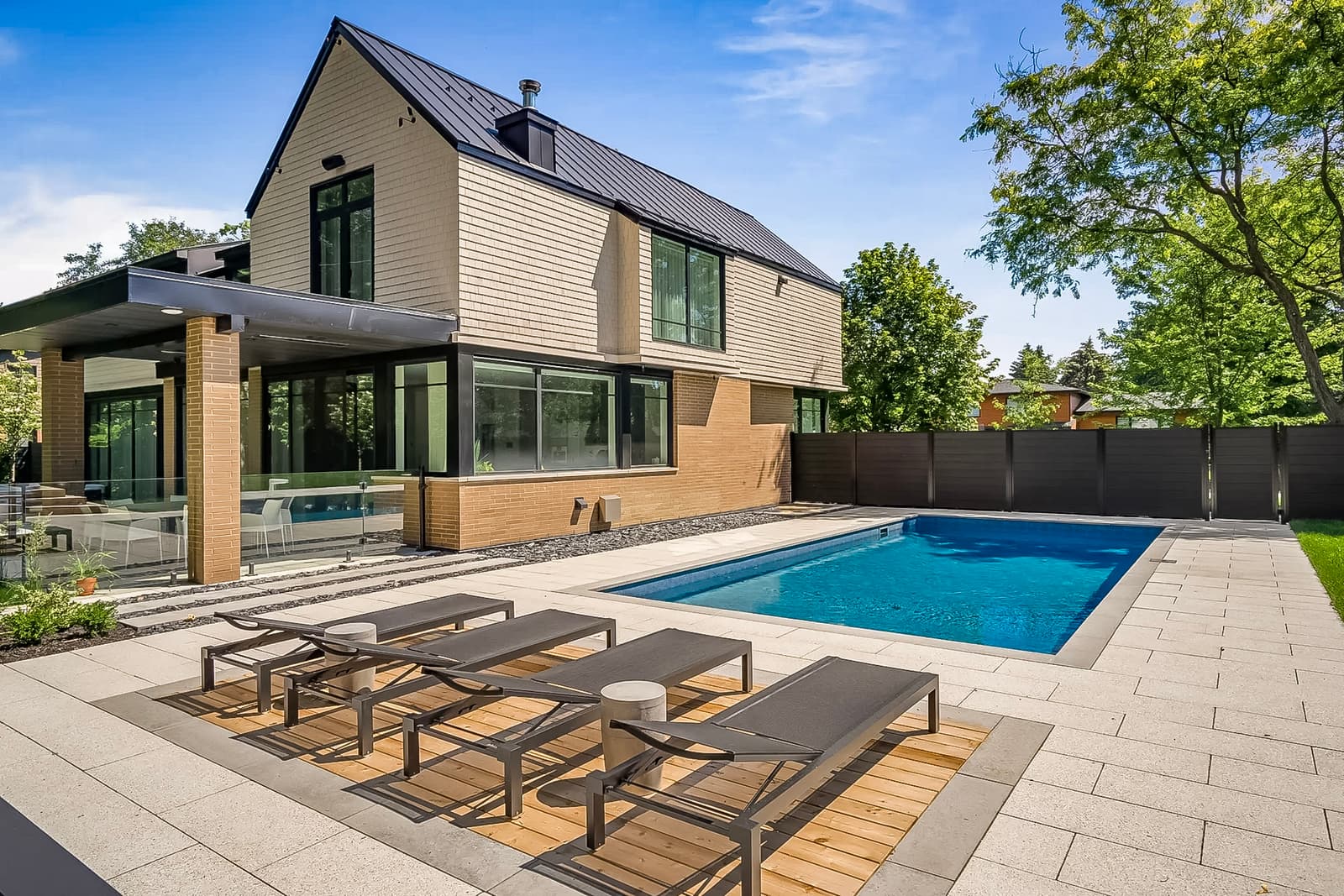Maison contemporaine avec piscine creusée, terrasse moderne et chaises longues, entourée de verdure.