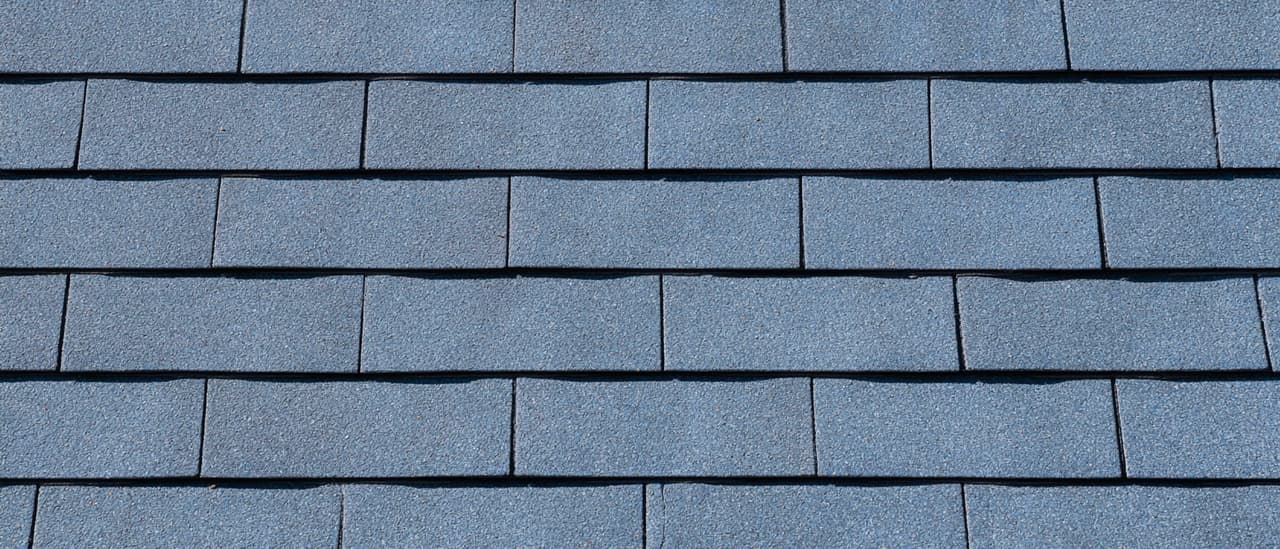 Vue rapprochée d'une toiture résidentielle recouverte de bardeaux d'asphalte gris bleuté, disposés en rangées horizontales régulières avec une texture granuleuse et une finition uniforme.