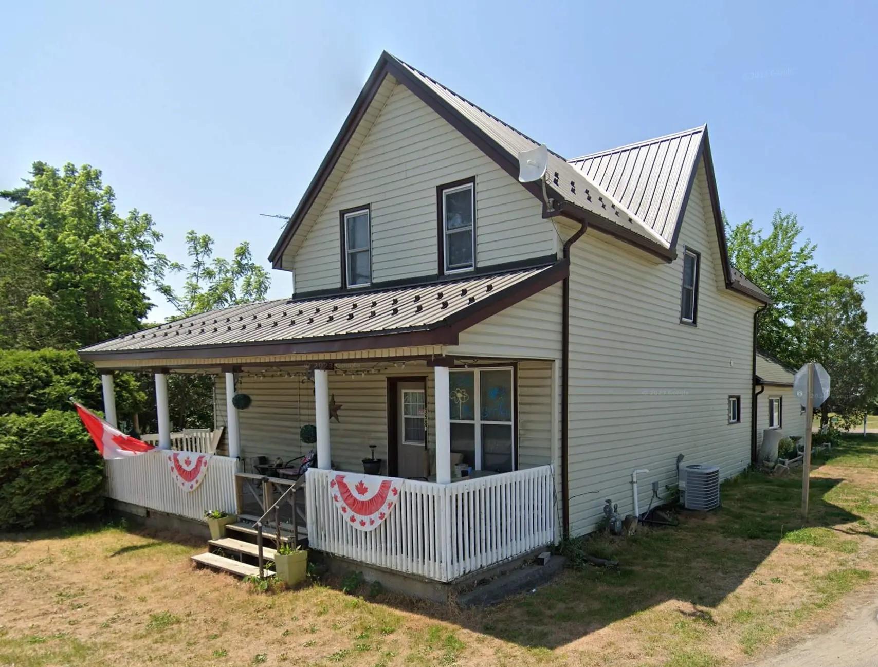 Maison à deux étages avec un toit en tôle métallique et une véranda, décorée pour la fête du Canada, située dans une rue résidentielle calme.