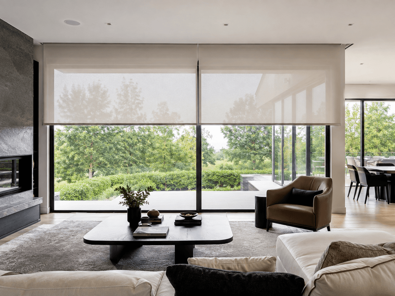Salon contemporain avec grandes portes vitrées, stores motorisés translucides, foyer moderne, mobilier minimaliste et vue sur un jardin verdoyant