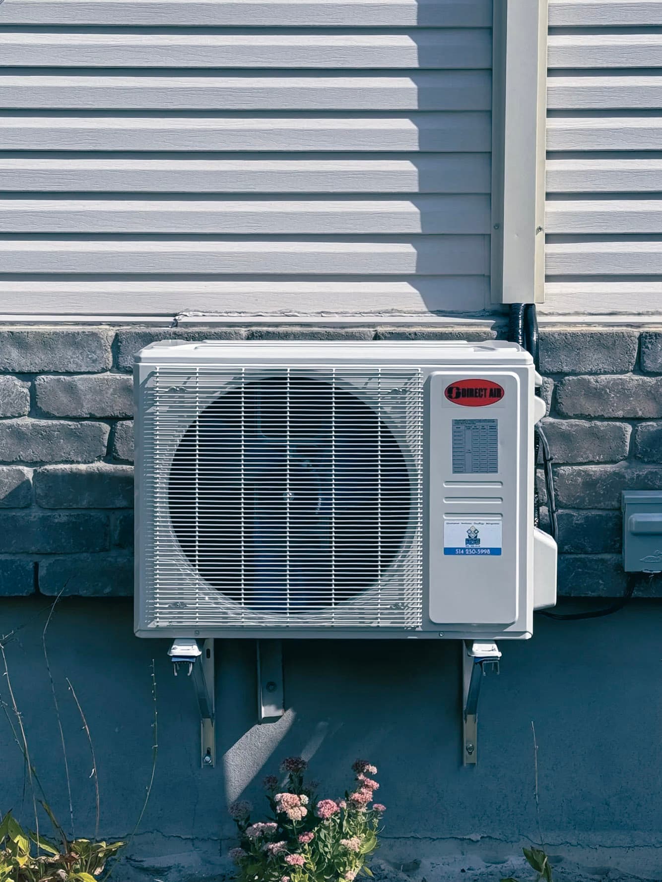 Thermopompe murale extérieure de marque Direct Air installée sur un mur de maison en pierre et vinyle