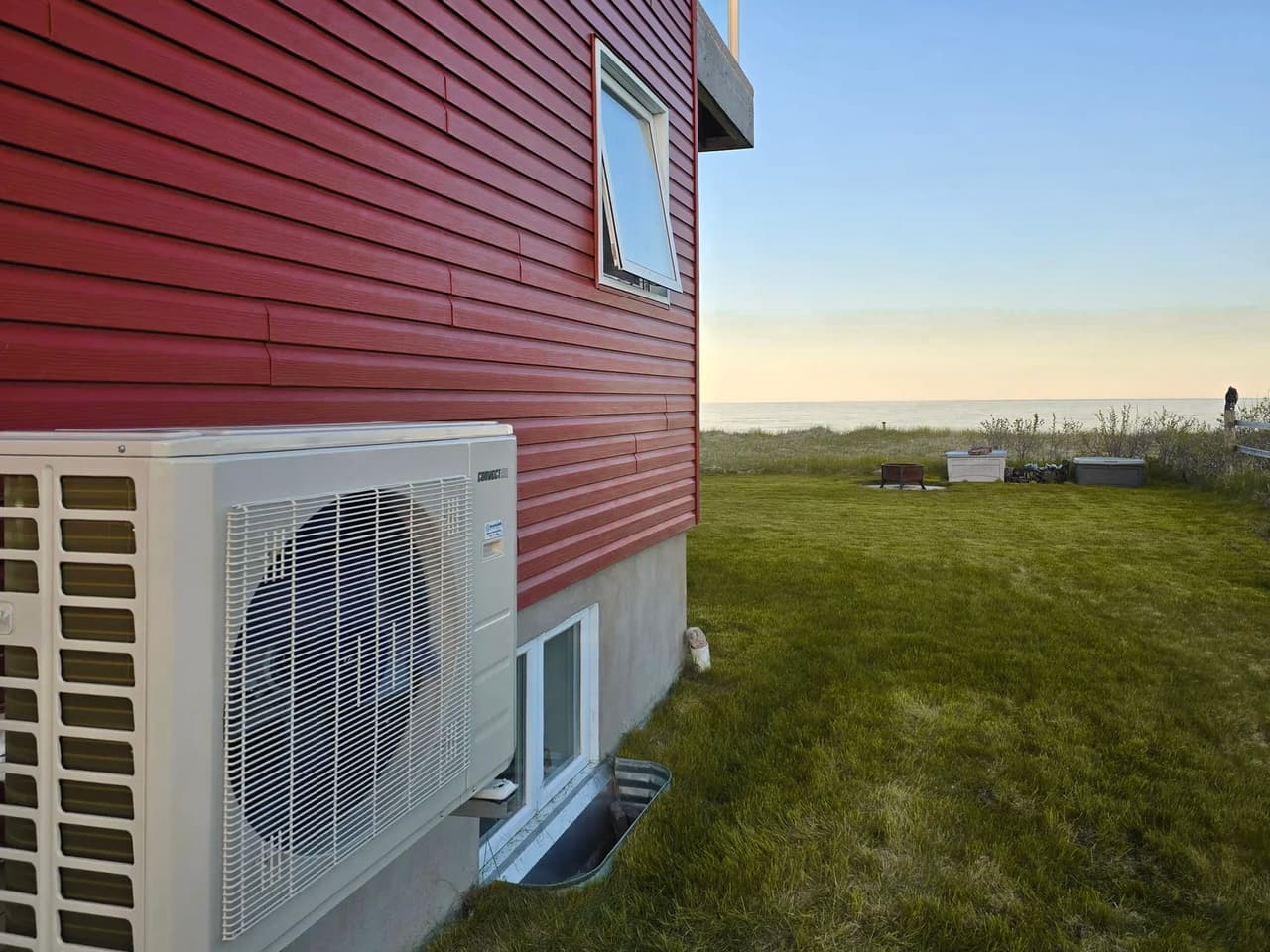 Unité de climatisation extérieure Samsung avec ventilateur, face à un jardin verdoyant et l'ocean
