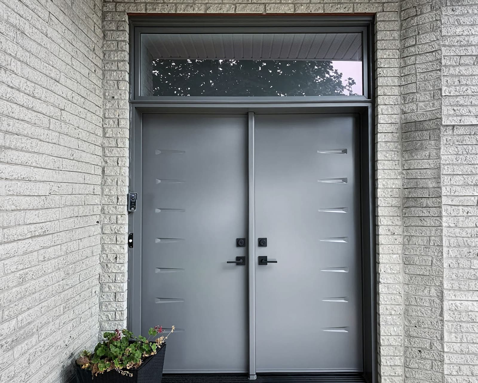 Double porte d'entrée moderne en acier avec poignées noires et panneau supérieur en verre dans une maison contemporaine.