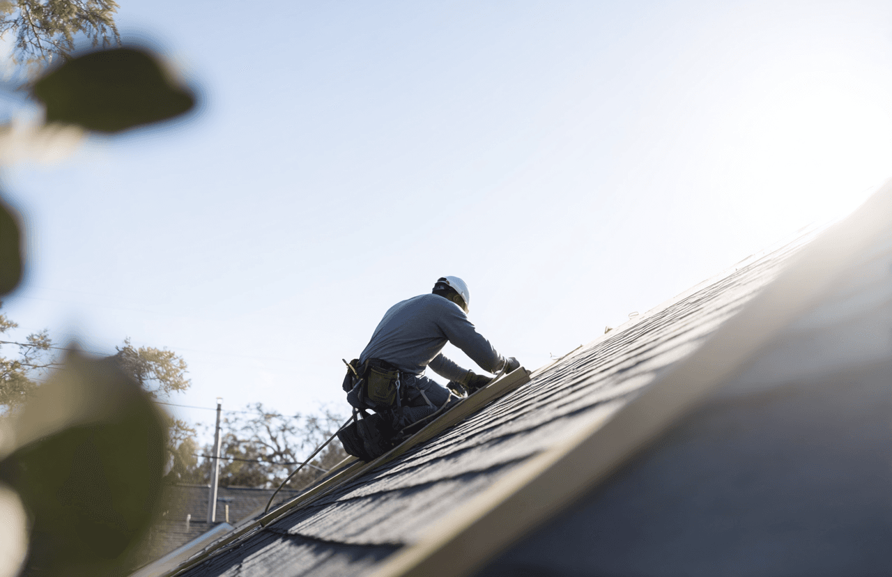 Ouvrier en casque de sécurité travaillant sur la toiture d’une maison sous un ciel ensoleillé