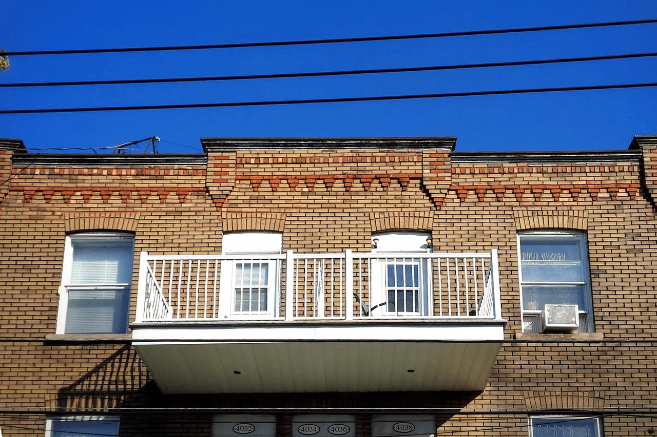 Façade en brique d’un immeuble résidentiel avec balcon blanc et fenêtres symétriques sous un ciel bleu clair