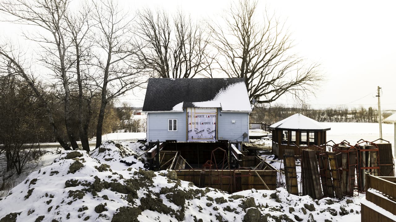 Maison surélevée avec travaux de coffrage et fondation en hiver dans un environnement rural enneigé pour agrandissement