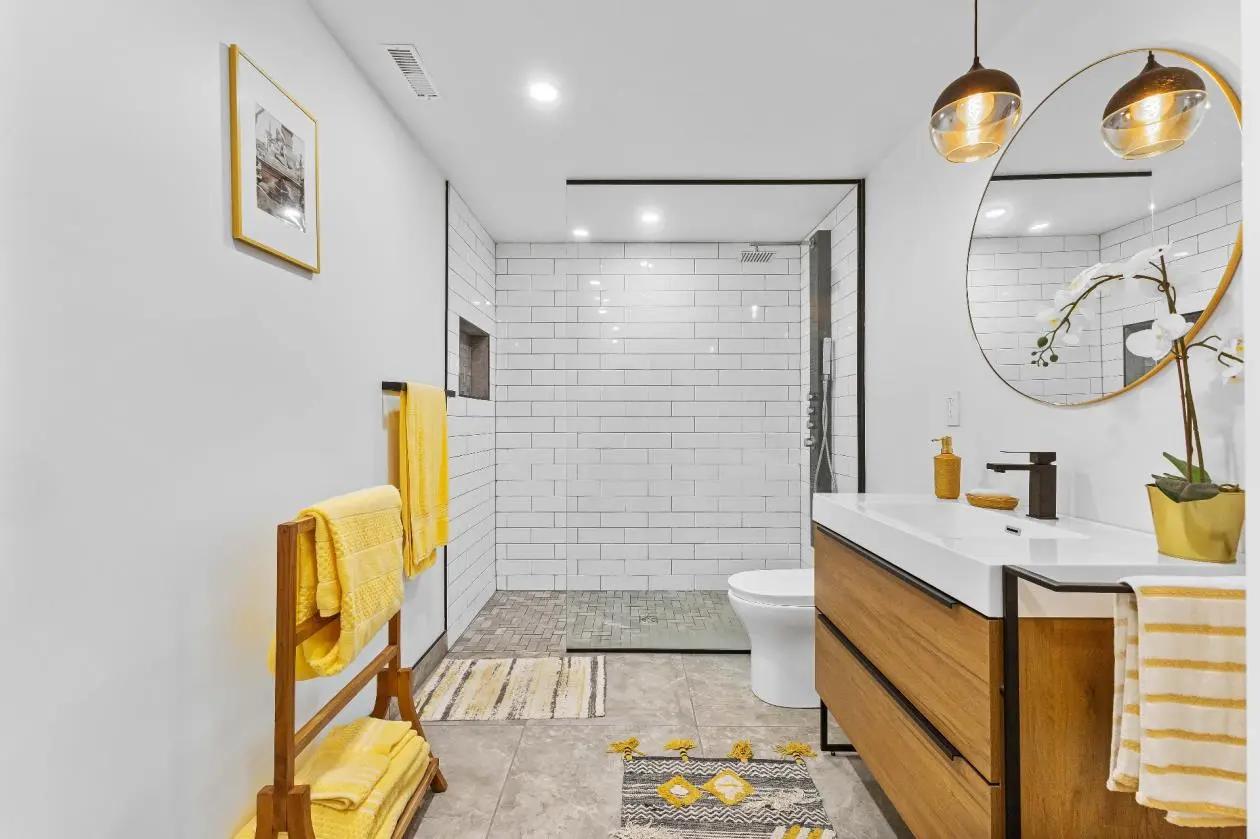 Salle de bain lumineuse avec une douche à l'italienne entourée de carreaux de métro blancs, une vasque posée sur un meuble en bois et un miroir rond