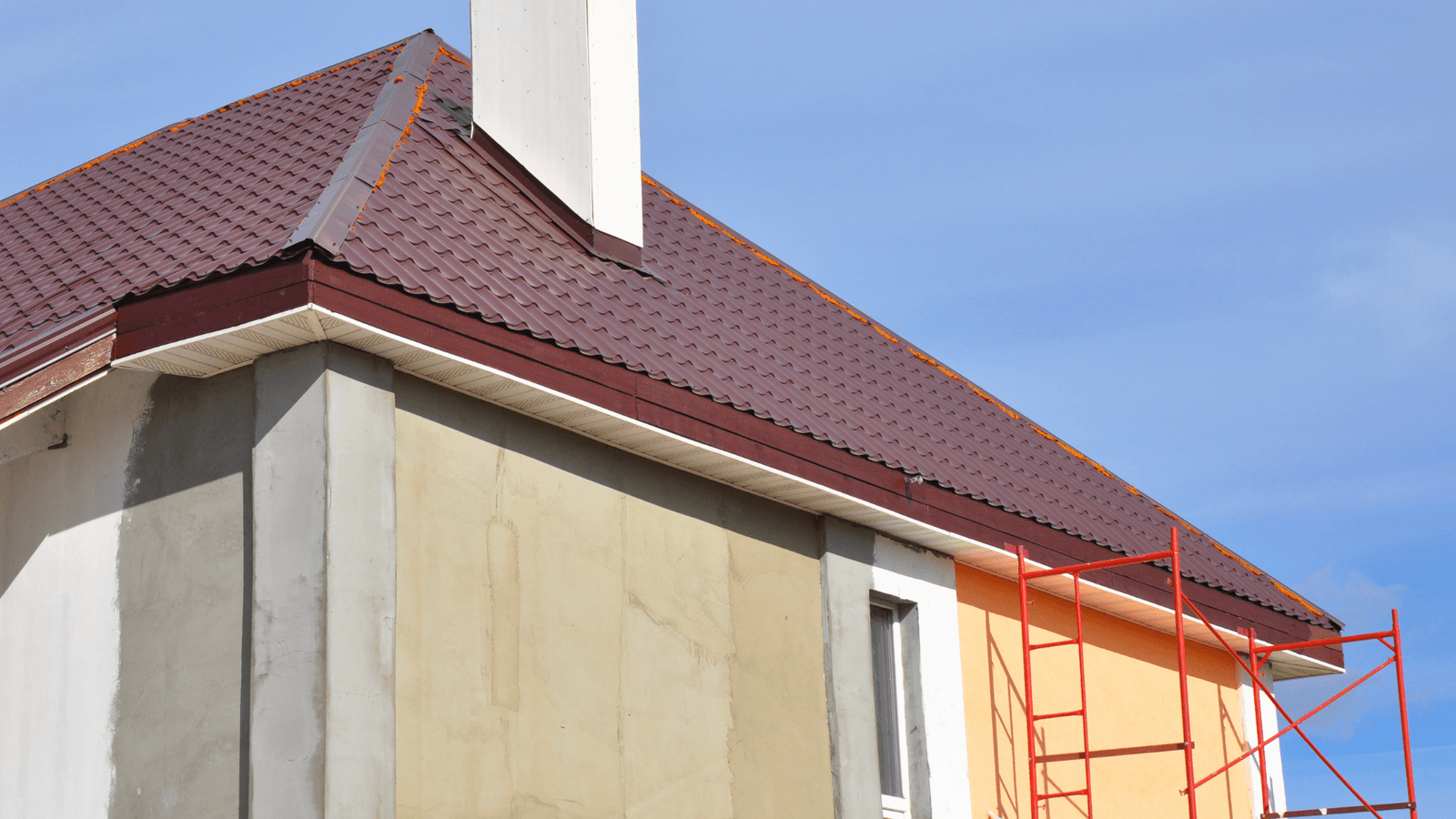 Une maison en construction avec un toit en métal brun et une cheminée blanche. L'extérieur de la maison est partiellement recouvert d'isolation et de panneaux de finition.