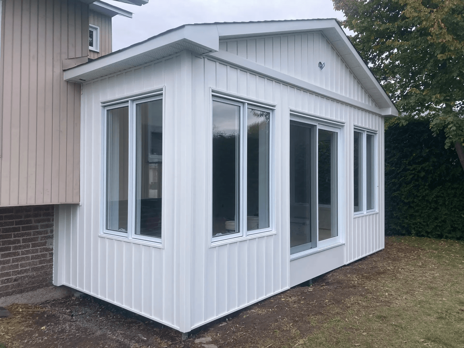 Agrandissement résidentiel moderne avec revêtement extérieur blanc, grandes fenêtres et porte vitrée donnant sur la cour arrière