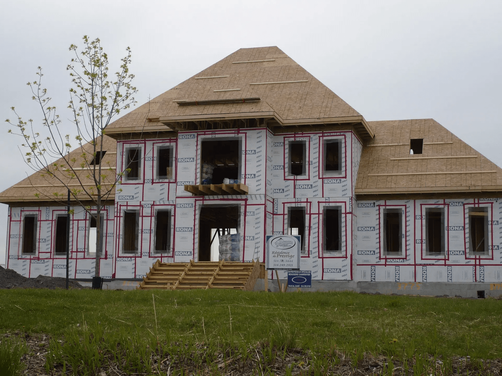 Maison résidentielle en construction avec charpente de toit, panneaux de bois, membrane pare-air et ouvertures de fenêtres avant la pose du revêtement extérieur