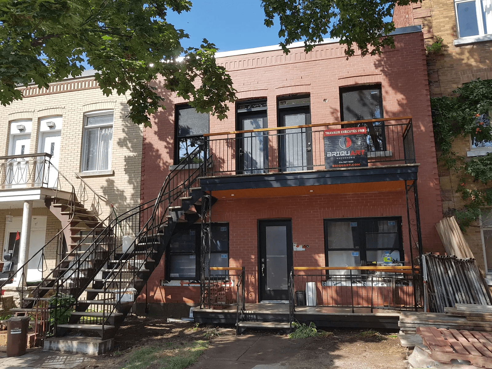 Rénovation de la façade en brique rouge d'un immeuble résidentiel de deux étages avec escaliers extérieurs en métal noir, balcons, portes et fenêtres modernes