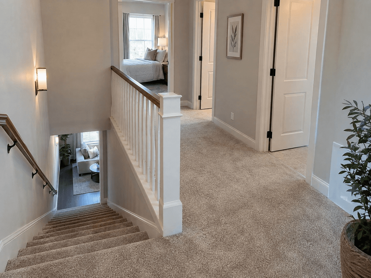 Palier d'étage lumineux avec escalier recouvert de moquette beige, rambarde blanche dotée d'une main courante en bois, portes intérieures blanches et accès aux chambres.