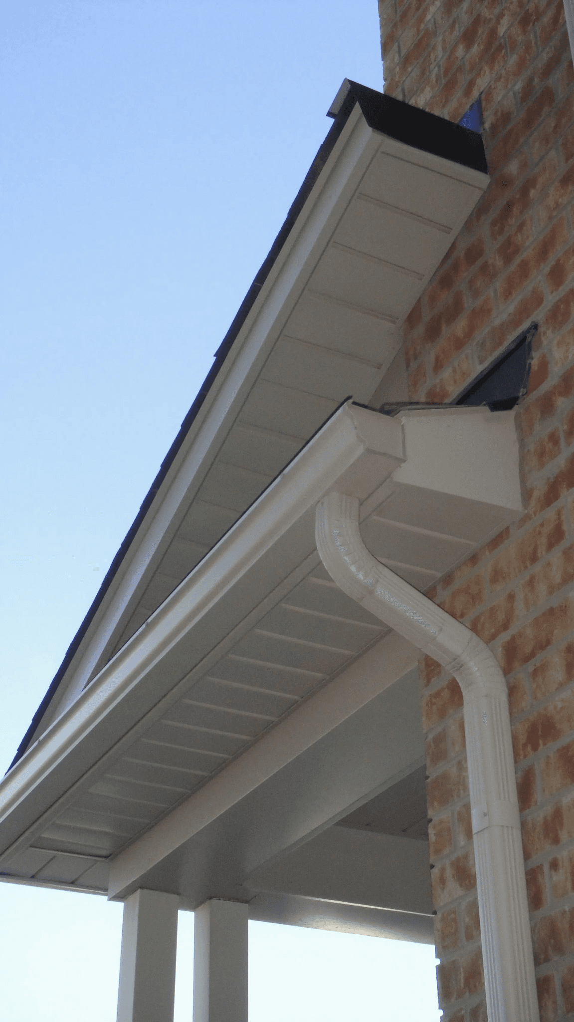 Gouttière blanche avec descente pluviale, soffite et fascia installés sur une maison en brique.