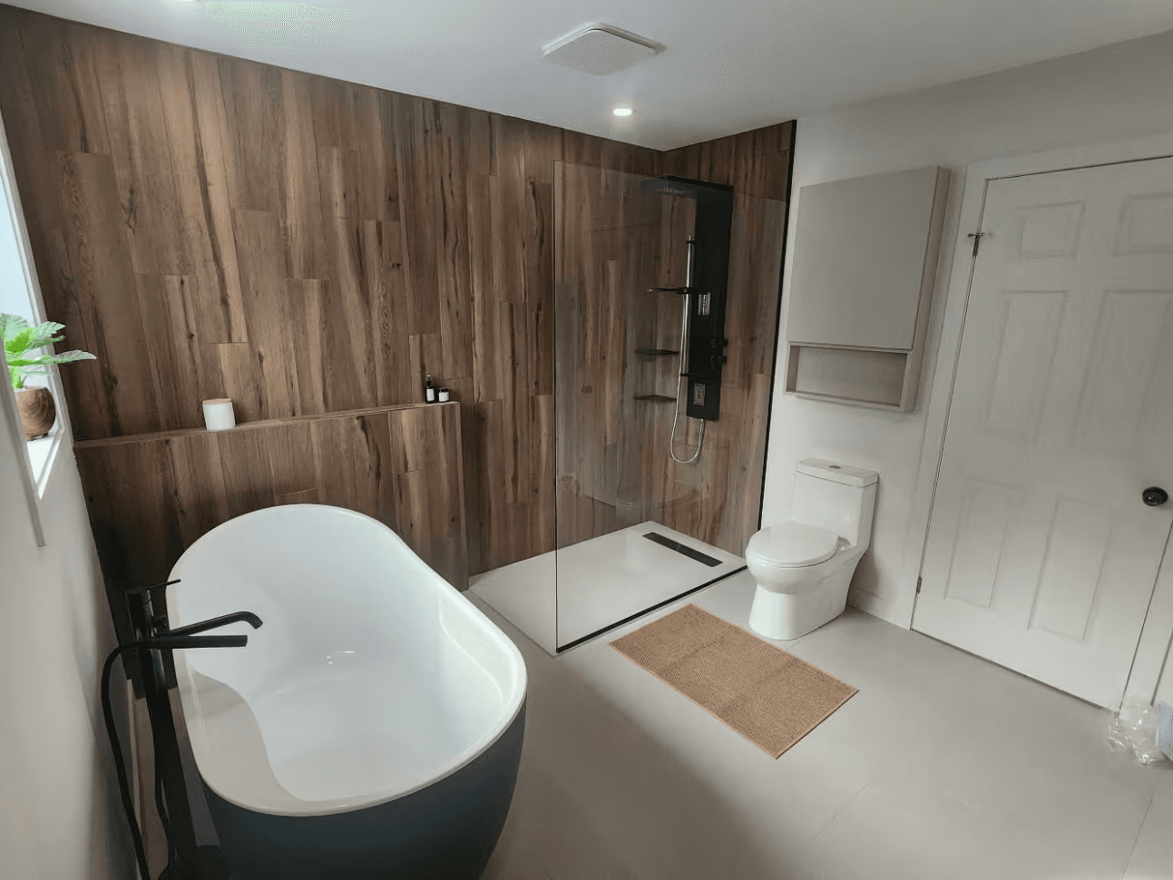 Salle de bain moderne avec baignoire autoportante, douche vitrée à l’italienne, revêtement mural effet bois, robinetterie noire et toilette blanche