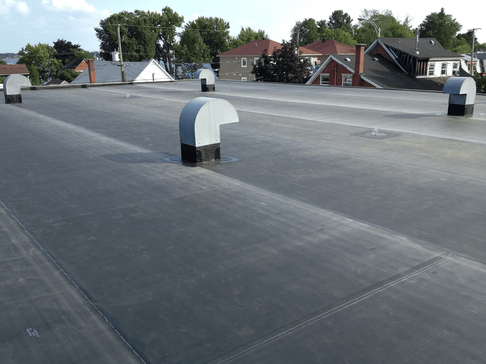 Toit plat recouvert d’une membrane d’étanchéité grise avec plusieurs sorties de ventilation, sur un bâtiment résidentiel en milieu urbain
