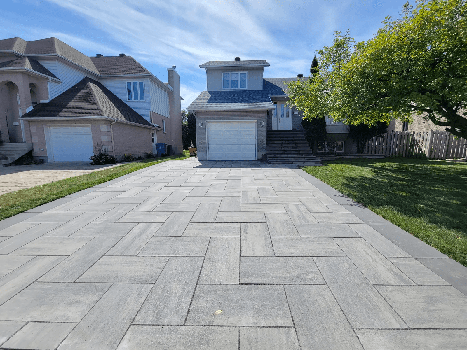 Entrée résidentielle moderne pavée en pavé-uni gris devant une maison de banlieue avec garage intégré