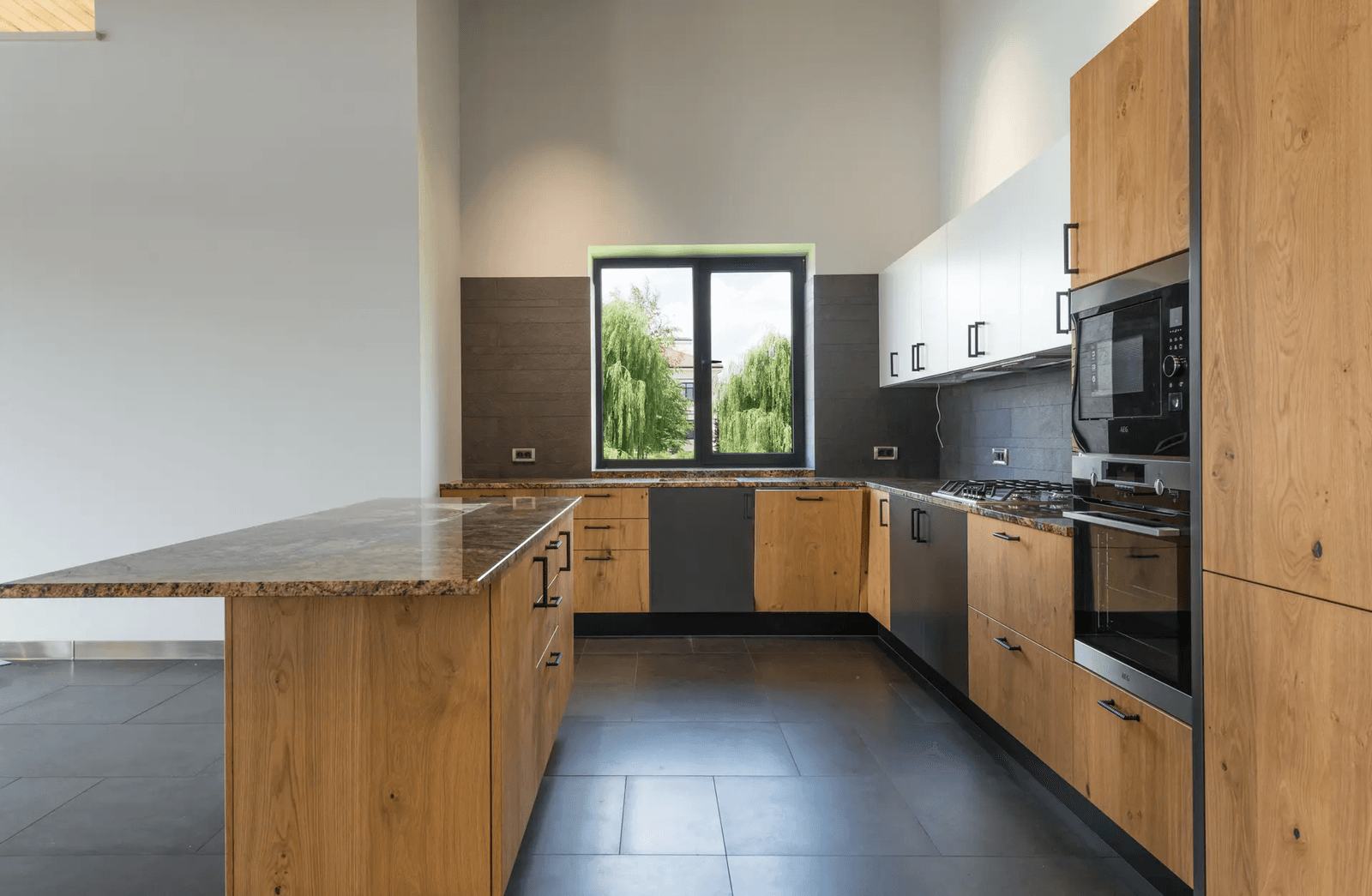 Cuisine moderne avec armoires en bois, comptoirs en granit, électroménagers intégrés et une grande fenêtre offrant une vue panoramique.
