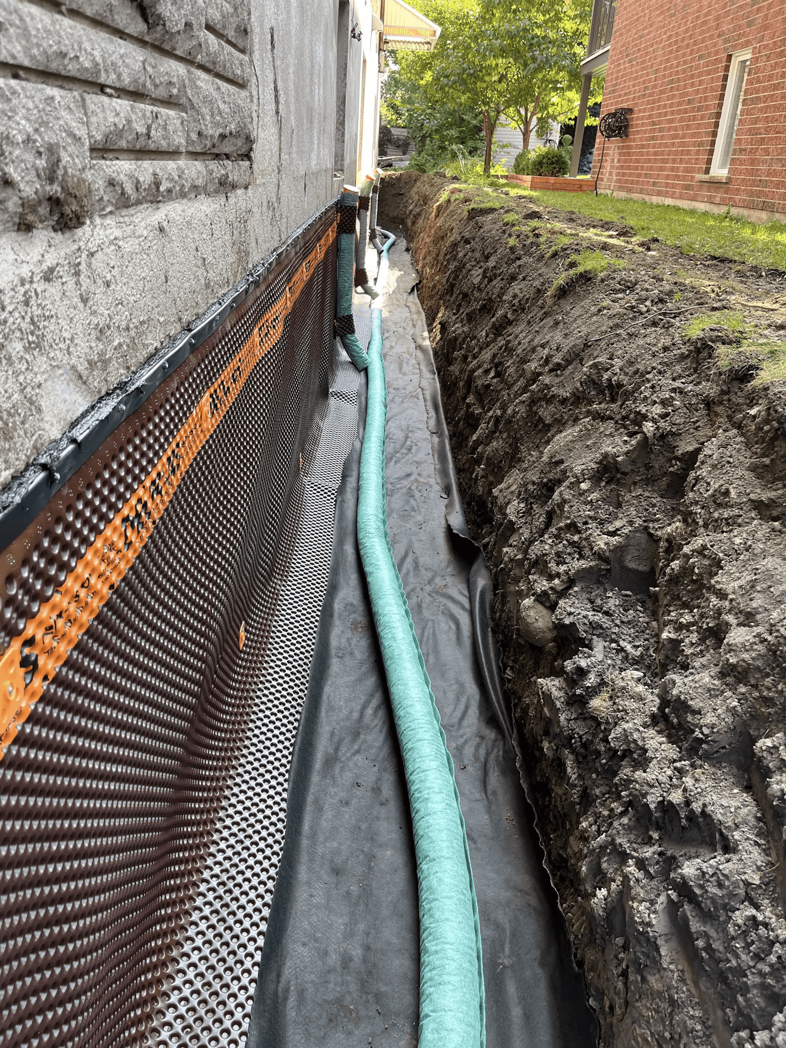 Installation d’un drain français avec membrane d’étanchéité le long des fondations d’une maison.