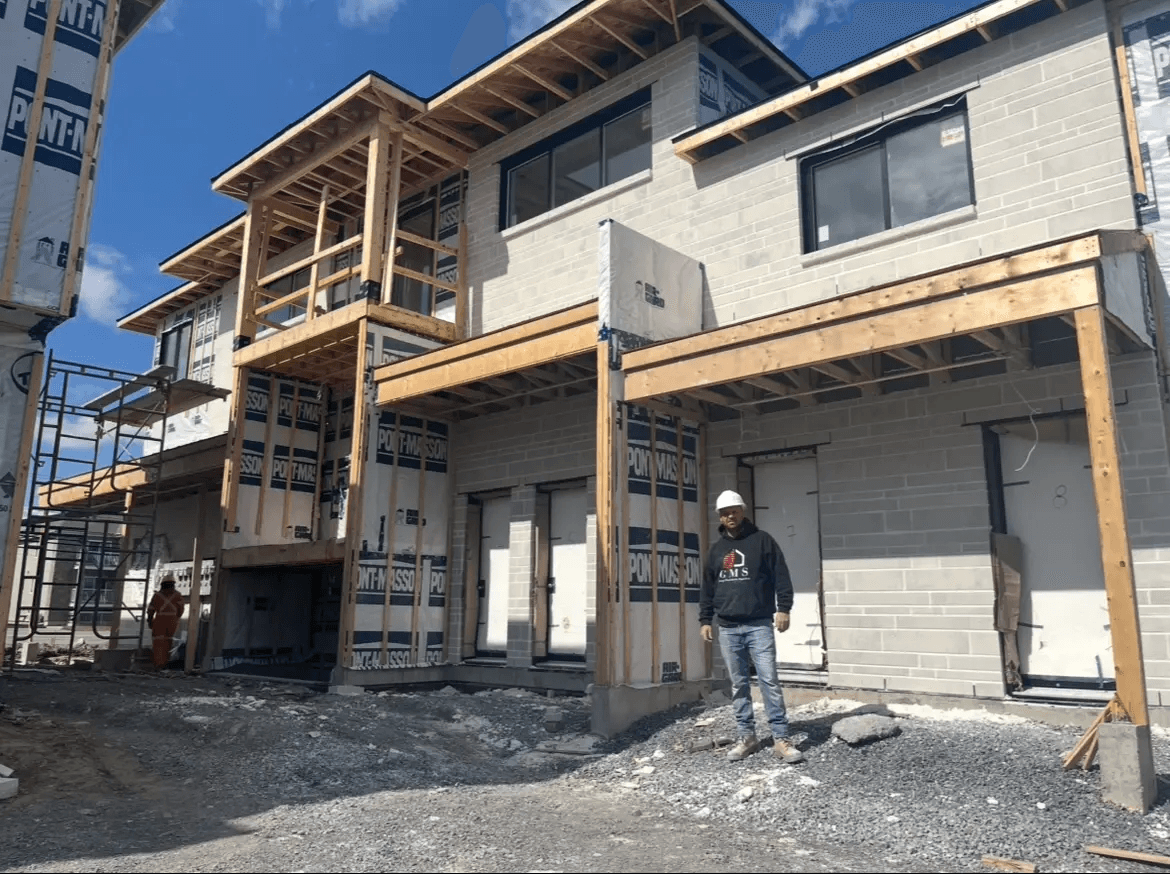 Construction d'un immeuble résidentiel multifamilial avec installation de maçonnerie extérieure en blocs gris, charpente de bois apparente, balcons en construction et travailleurs sur le chantier