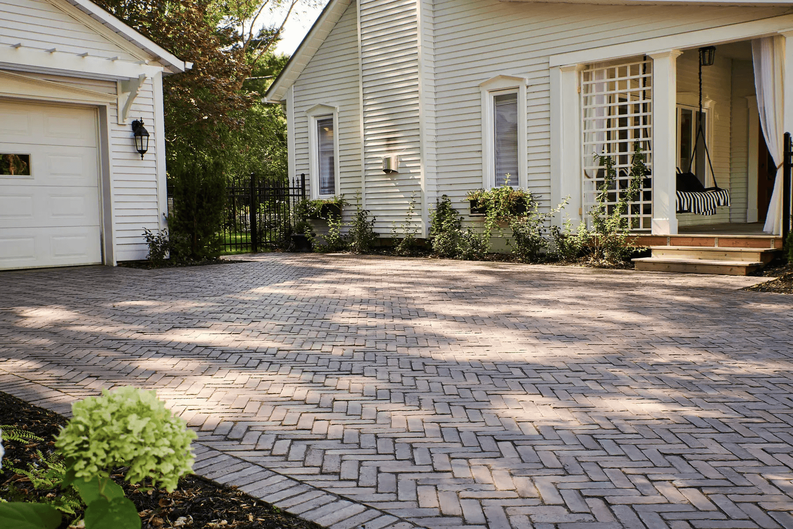 Entrée de maison en pavé-uni de style brique avec aménagement paysager devant une résidence blanche.