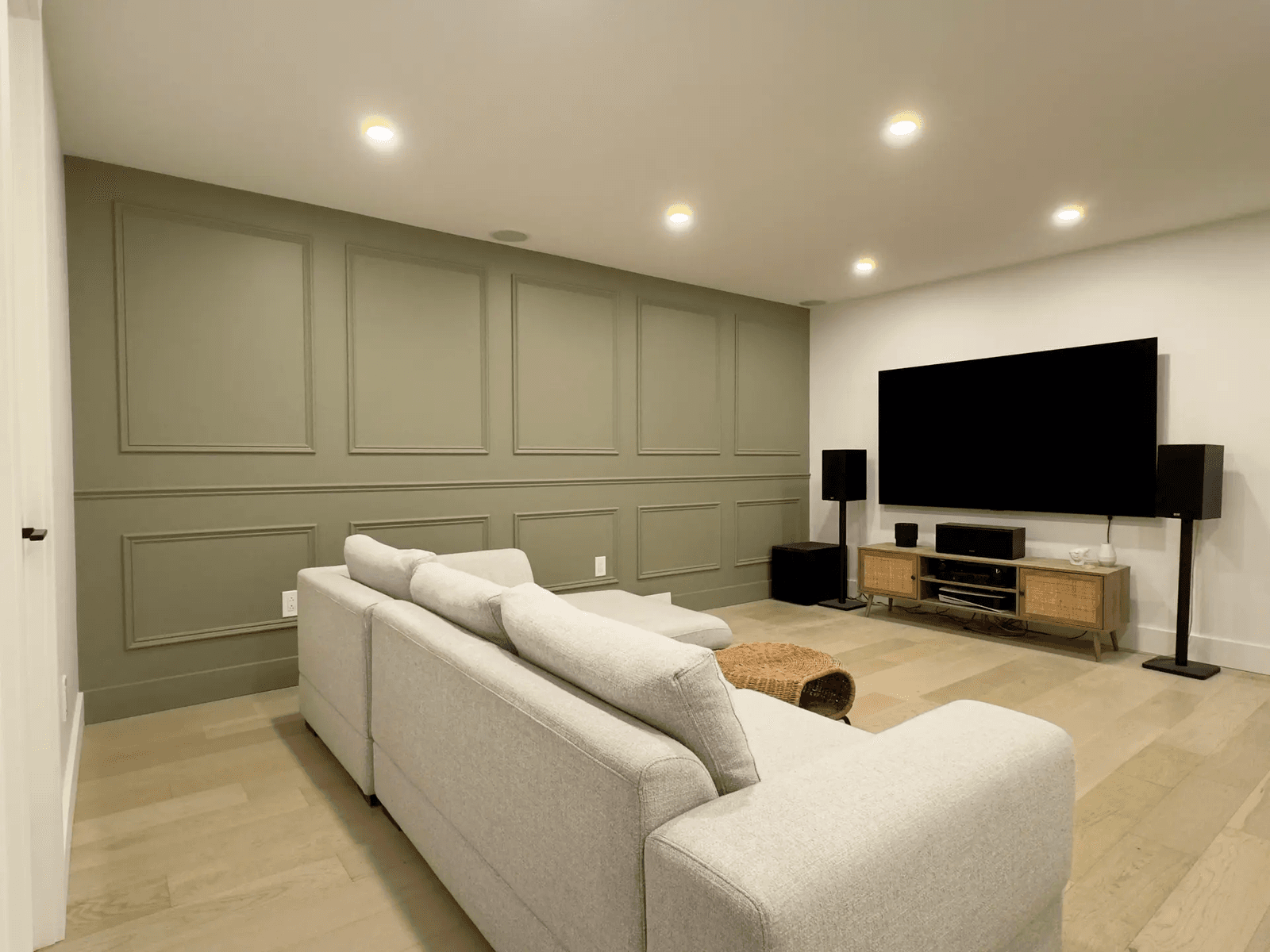 Salon moderne en sous-sol avec un mur accent vert, un grand canapé gris, un téléviseur écran plat et un système audio.&nbsp;