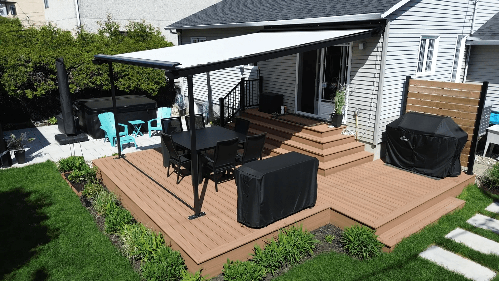 Terrasse en composite avec auvent rétractable, coin repas et spa extérieur. /&nbsp;Composite deck with retractable awning, dining area, and outdoor hot tub.