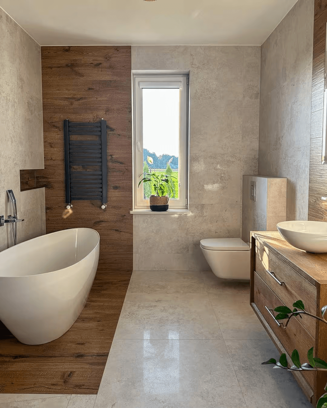 Salle de bain contemporaine avec baignoire autoportante blanche, revêtement mural imitation bois brun, grands carreaux de céramique beige effet pierre, toilette suspendue, meuble-lavabo en bois naturel, vasque blanche, sèche-serviettes noir et fenêtre lumineuse