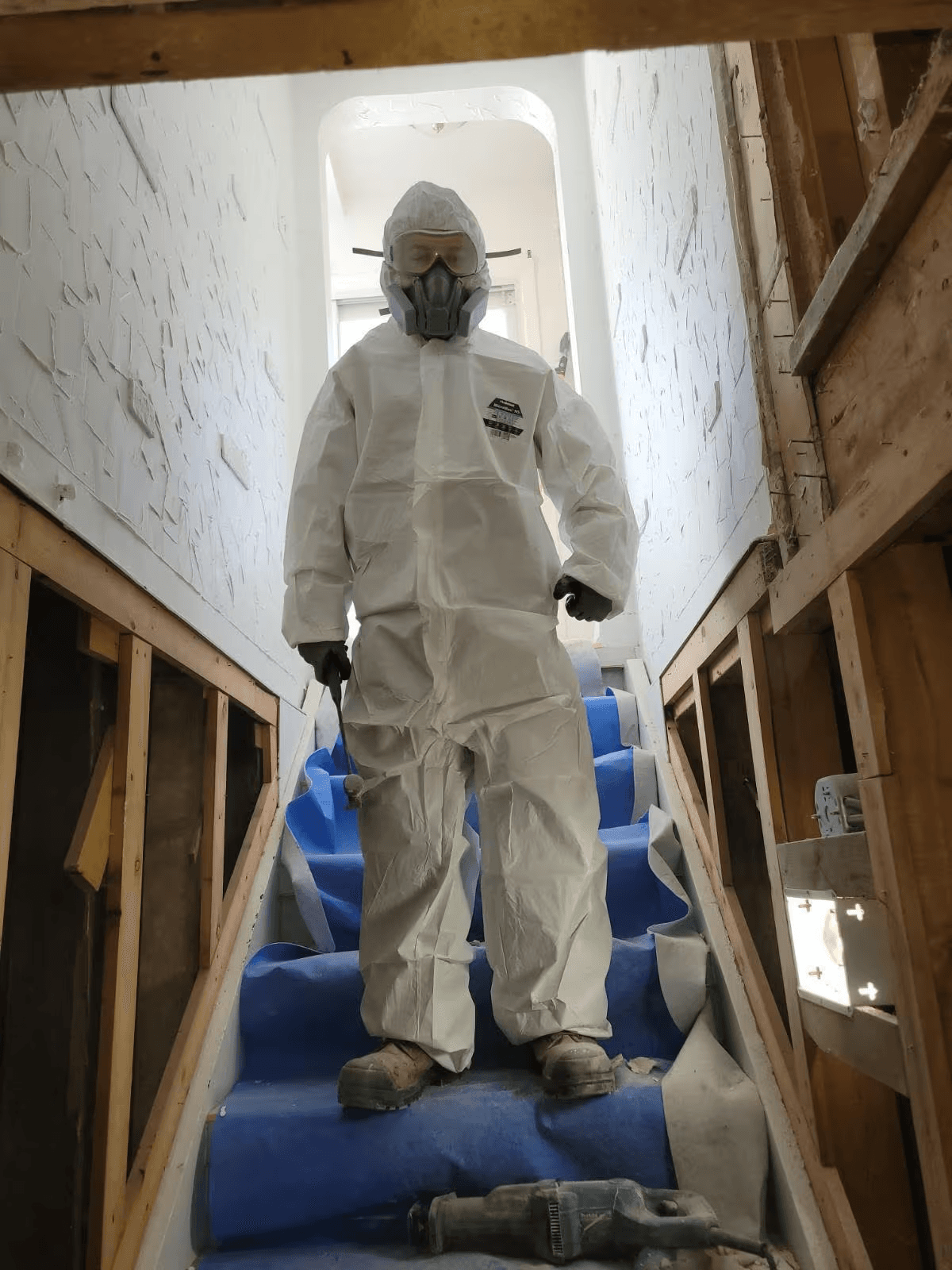 &nbsp;Travailleur en combinaison de protection avec respirateur sur un escalier en rénovation, entouré de murs ouverts et de charpente apparente /&nbsp;Worker wearing a protective suit and respirator on a staircase under renovation, surrounded by open walls and exposed framing&nbsp;